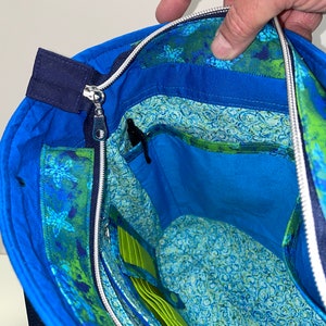 May include: A blue tote bag with a zipper closure and a green and blue floral lining. The bag has a zipped pocket and a slip pocket inside.