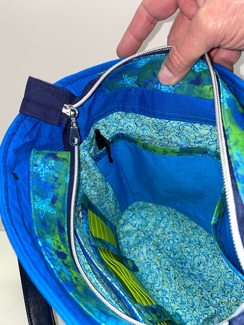 May include: A blue tote bag with a zipper closure and a green and blue floral lining. The bag has a zipped pocket and a slip pocket inside.