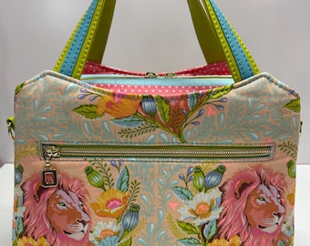 May include: A floral patterned handbag with a lion's head design. The bag features a peach background with a repeating pattern of flowers and leaves. The handles are green with blue and yellow accents. The bag has a gold zipper and a pink interior.