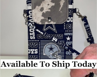 May include: A blue and white crossbody phone bag with a Dallas Cowboys theme. The bag has a large star and the words "Cowboys" printed on it. The bag has a small pocket on the front with a cowhide pattern.