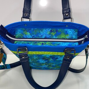 May include: A blue and green tote bag with a sea turtle print and navy blue handles. The bag has a zippered top closure and a lime green stripe.