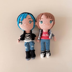 May include: Two handmade crochet dolls. One doll has blue hair, a black jacket, and blue jeans. The other doll has brown hair, a gray jacket, a red shirt with "JAN" on it, and blue jeans. Both dolls have black boots.