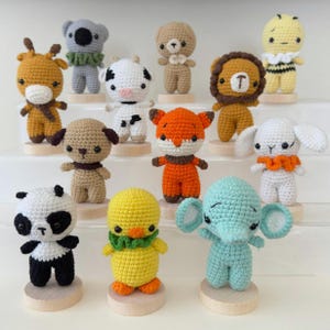 May include: A collection of handmade crochet animal figurines, including a giraffe, koala, bear, cow, fox, lion, bee, dog, bunny, panda, duck, and elephant. Each animal is crafted with colorful yarn and stands on a small wooden base.
