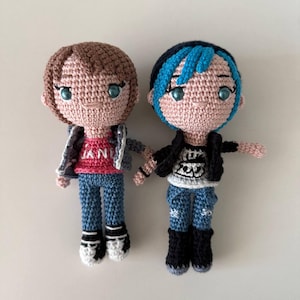 May include: Two handmade crochet dolls, each with a unique hairstyle and outfit. One doll has brown hair and a pink shirt, the other has blue-streaked hair and a black jacket. Both dolls wear blue jeans and black boots.