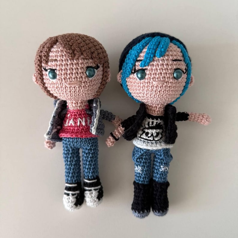 May include: Two handmade crochet dolls, each with a unique hairstyle and outfit. One doll has brown hair and a pink shirt, the other has blue-streaked hair and a black jacket. Both dolls wear blue jeans and black boots.