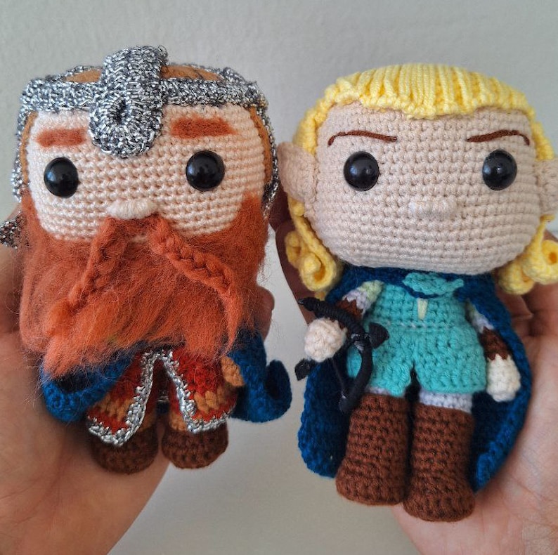 May include: Two crocheted plush toys, one a dwarf with a red beard and a blue and gold tunic, the other an elf with blonde hair and a blue and green tunic.