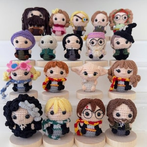Puede incluir: Una colección de muñecos de ganchillo hechos a mano, cada uno representando a un personaje de una popular serie de fantasía. Los muñecos presentan rasgos faciales, ropa y accesorios detallados, incluyendo gafas, bufandas y sombreros. Los muñecos se exhiben sobre pequeños soportes de madera.