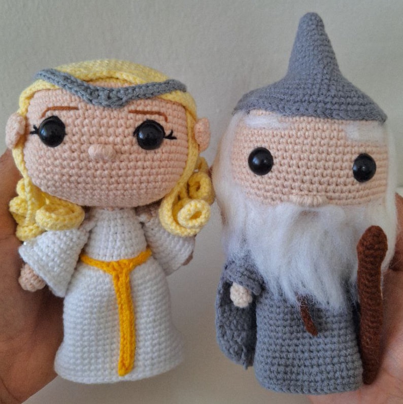 May include: Two crocheted amigurumi dolls, one a female figure with blonde hair and a white dress, the other a male figure with a grey beard and a grey robe and hat.
