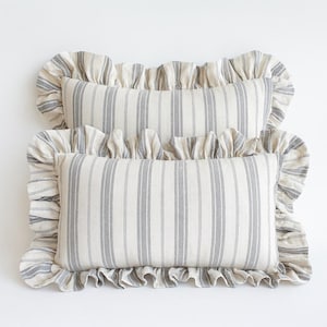 Op de afbeelding: Twee rechthoekige kussens met een gestreept patroon in grijs en gebroken wit. De kussens hebben gerimpelde randen, wat een decoratief tintje geeft. De kussens zijn ontworpen voor woondecoratie en voegen een vleugje elegantie toe aan elke kamer.