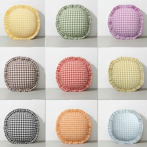 Puede incluir: Nueve cojines redondos decorativos en varios colores, cada uno con un estampado de cuadros y bordes con volantes. Los colores incluyen amarillo, verde, morado, marrón, rojo, amarillo claro, negro, naranja y azul. Los cojines están dispuestos en una cuadrícula.