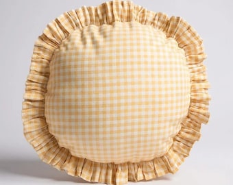 May include: A round decorative pillow with a yellow and white gingham pattern. The pillow has a ruffled edge in a matching yellow fabric, creating a textured and stylish accent for home decor.