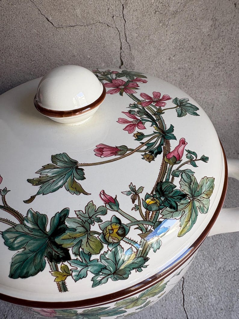 Peut inclure: Un plat de service en c&eacute;ramique blanche avec un couvercle et une poign&eacute;e. Le couvercle comporte un bouton blanc avec un bord marron. Le plat est d&eacute;cor&eacute; d'un motif floral rose, vert et marron. Le plat est probablement utilis&eacute; pour servir des aliments.