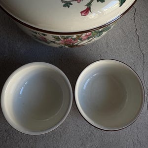 Peut inclure: Un grand bol de service en c&eacute;ramique cr&egrave;me avec un motif floral rose et vert, et deux petits bols assortis. Les bols ont une bordure marron fonc&eacute;. Le motif floral est sur le couvercle du bol.