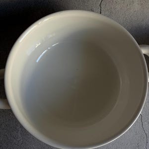 Peut inclure: Un bol en c&eacute;ramique blanc cr&egrave;me avec deux petites poign&eacute;es. Le bol a une finition lisse et brillante et une conception large et peu profonde. L'int&eacute;rieur est blanc vif et l'ext&eacute;rieur est l&eacute;g&egrave;rement blanc cass&eacute;.