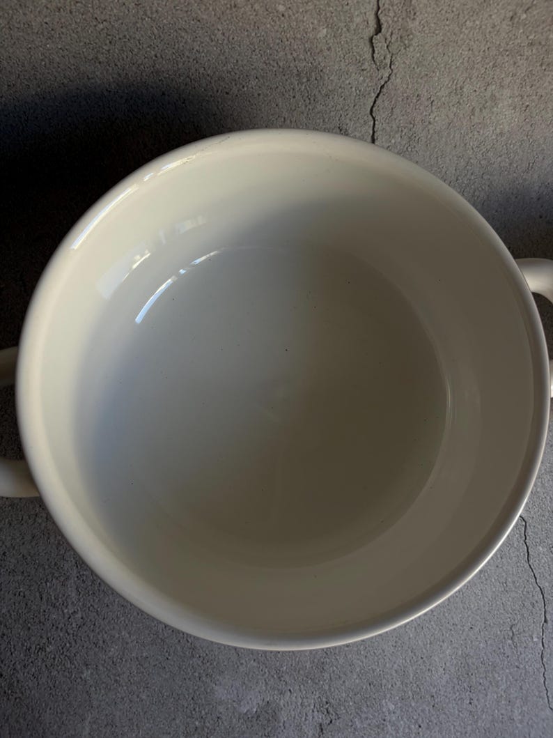 Peut inclure: Un bol en c&eacute;ramique blanc cr&egrave;me avec deux petites poign&eacute;es. Le bol a une finition lisse et brillante et une conception large et peu profonde. L'int&eacute;rieur est blanc vif et l'ext&eacute;rieur est l&eacute;g&egrave;rement blanc cass&eacute;.