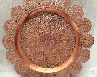Könnte beinhalten: Ein kupferfarbenes Ziertablett mit einem komplizierten Blumenmuster. Das Tablett hat einen gewellten Rand und ein detailliertes Design in der Mitte. Das Metall hat einen warmen, rötlich-braunen Farbton, und das Design ist aufwendig und detailliert.