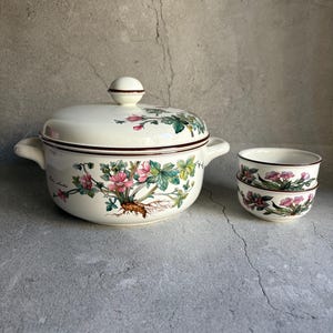 Peut inclure: Un service de table en c&eacute;ramique cr&egrave;me comprenant un grand bol avec couvercle et deux petits bols assortis. Le motif floral pr&eacute;sente des fleurs roses, des feuilles vertes et des bordures marron.