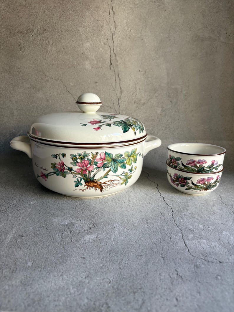 Peut inclure: Un service de table en c&eacute;ramique cr&egrave;me comprenant un grand bol avec couvercle et deux petits bols assortis. Le motif floral pr&eacute;sente des fleurs roses, des feuilles vertes et des bordures marron.