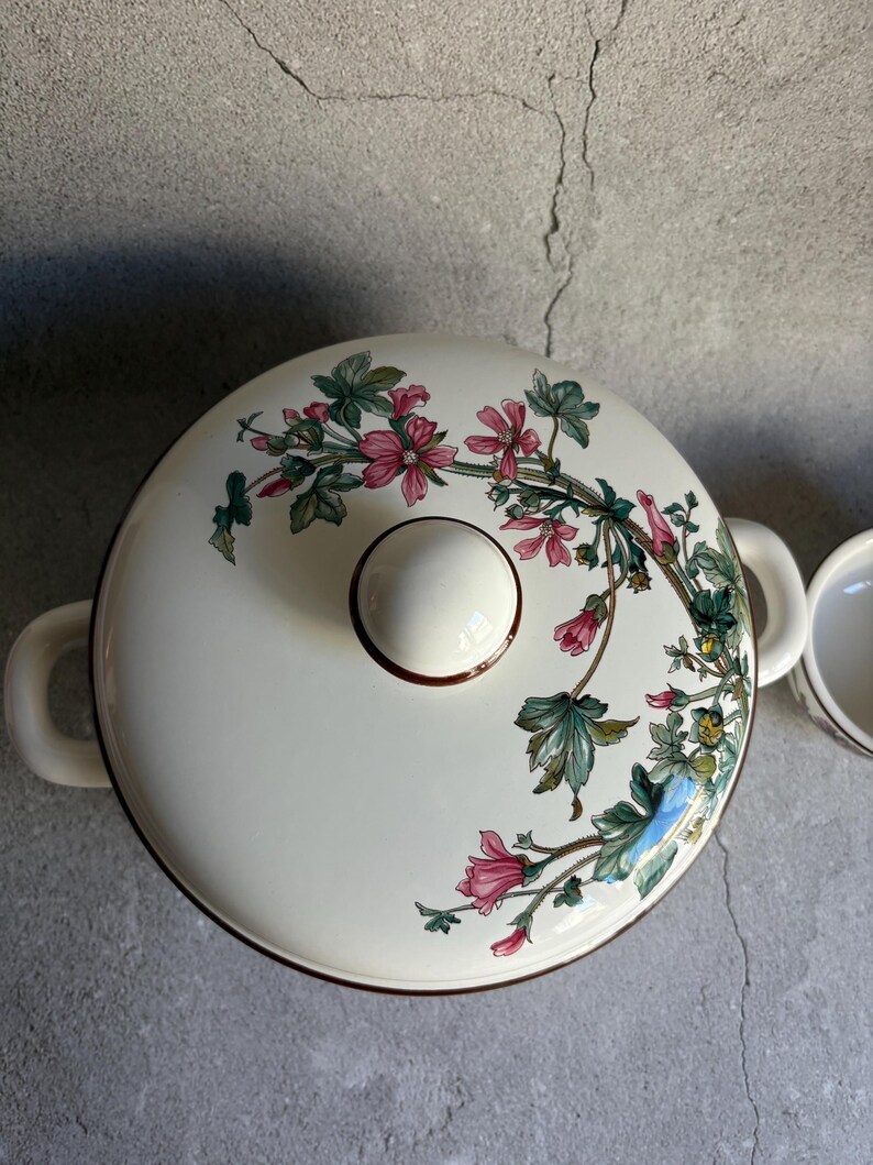 Peut inclure: Plat &agrave; four en c&eacute;ramique cr&egrave;me avec couvercle. Le couvercle pr&eacute;sente un motif floral avec des fleurs roses et des feuilles vertes. Le plat a deux poign&eacute;es et un bouton rond. Mesures en cm.