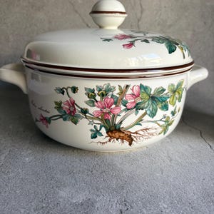 Peut inclure: Un plat de service en c&eacute;ramique blanche avec un couvercle, orn&eacute; d'un motif floral rose, vert et marron. Le plat a deux poign&eacute;es et un bouton sur le couvercle. Le bord et le bouton sont marron. Vintage.