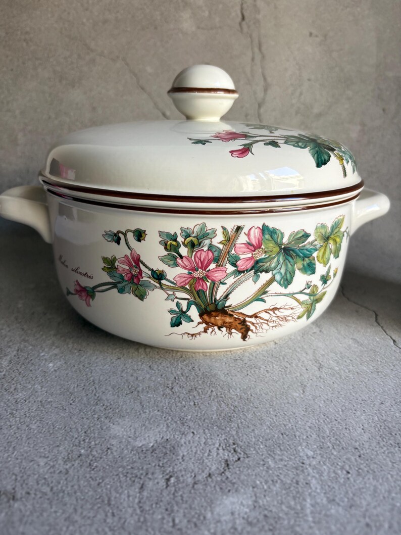 Peut inclure: Un plat de service en c&eacute;ramique blanche avec un couvercle, orn&eacute; d'un motif floral rose, vert et marron. Le plat a deux poign&eacute;es et un bouton sur le couvercle. Le bord et le bouton sont marron. Vintage.