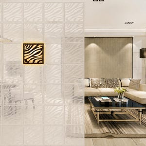 Puede incluir: Un biombo divisor compuesto por paneles cuadrados con un patrón de rayas de cebra blanco translúcido. Un aplique de pared cuadrado con marco negro y un diseño de rayas de cebra amarillo brillante está montado en el centro de la pantalla.