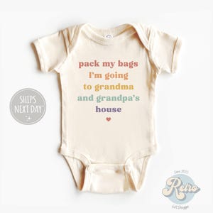 May include: A cream-colored baby onesie with the text "pack my bags I'm going to grandma and grandpa's house" in rainbow colors. A small red heart is below the text.