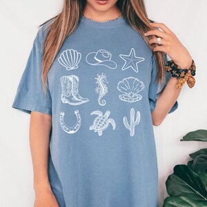 woman wearing a blue jean shirt with rows of cowgirl and coastal elements.