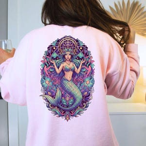 May include: Light pink sweatshirt featuring a colorful mermaid graphic on the back. The mermaid has long flowing hair, a crown, and a detailed tail. The design includes shades of blue, purple, and green, with the text "LIGHT PINK" at the bottom.