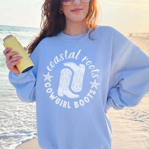 May include: Light blue sweatshirt with a white graphic design that says "coastal roots cowgirl boots" with a pair of cowboy boots in the center.