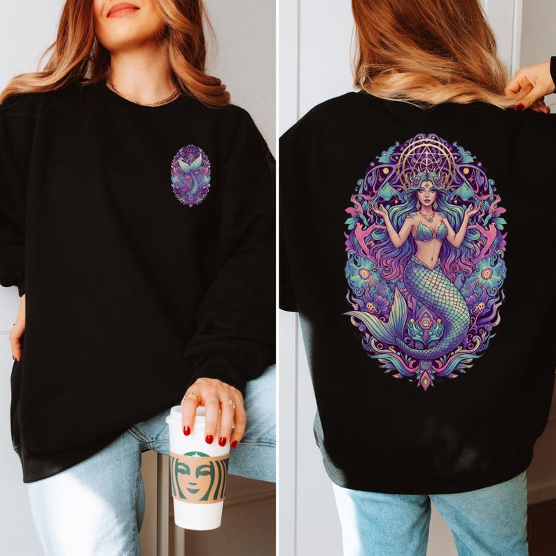 May include: Black sweatshirt with a mermaid design. The front features a small, oval-shaped mermaid tail design in purple and blue. The back displays a larger, detailed illustration of a mermaid with flowing hair, a crown, and a teal tail, surrounded by floral elements.