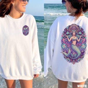 May include: White sweatshirt featuring a mermaid design. The front has a small oval graphic of a mermaid tail. The back displays a large, colorful illustration of a mermaid with flowing hair, a crown, and a detailed background. The word "WHITE" is at the bottom.
