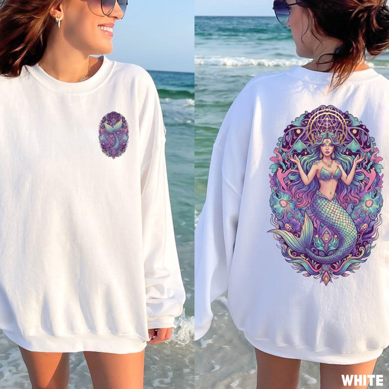 May include: White sweatshirt featuring a mermaid design. The front has a small oval graphic of a mermaid tail. The back displays a large, colorful illustration of a mermaid with flowing hair, a crown, and a detailed background. The word "WHITE" is at the bottom.