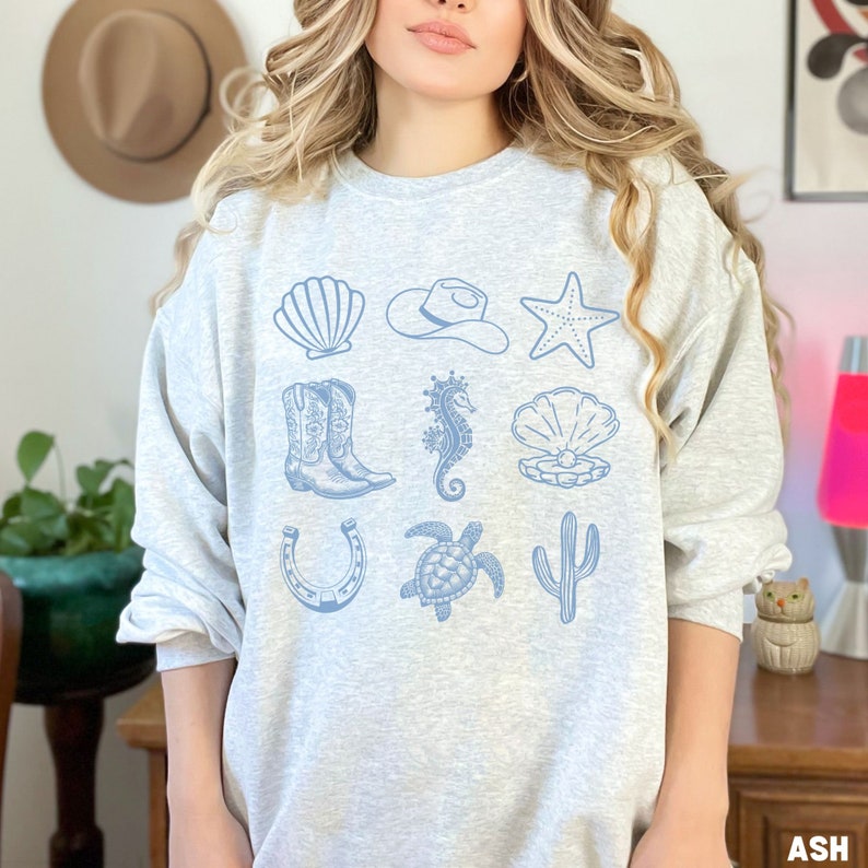 woman wearing the ash  sweatshirt with rows of western and ocean elements in blue design.