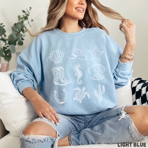 woman wearing the light blue sweatshirt with rows of western and ocean elements in white design.