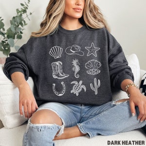 woman wearing the dark heather sweatshirt with rows of western and ocean elements in white design.
