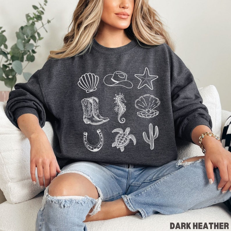 woman wearing the dark heather sweatshirt with rows of western and ocean elements in white design.