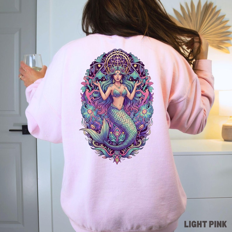 May include: Light pink sweatshirt featuring a colorful mermaid graphic on the back. The mermaid has long flowing hair, a crown, and a detailed tail. The design includes shades of blue, purple, and green, with the text "LIGHT PINK" at the bottom.