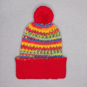 Double- layered multicolor beanie hat with red brim and bobble lying flat.
