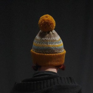 Beanie with folded brim and one Pom Pom in mustard and sand and blue colors.