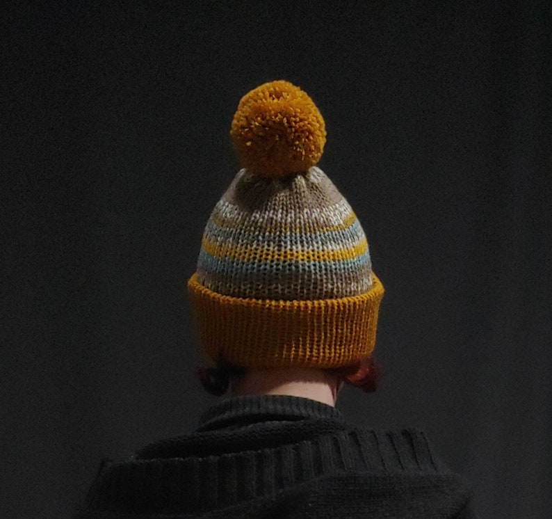 Beanie with folded brim and one Pom Pom in mustard and sand and blue colors.