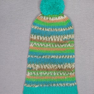 A slouchy warm hat with one bobble in green, yellow nad mint colors laying flat.