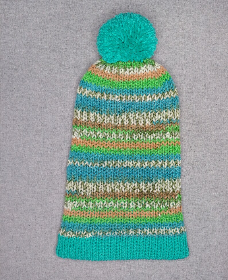 A slouchy warm hat with one bobble in green, yellow nad mint colors laying flat.