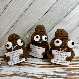 May include: Three brown crocheted poop figures with large white eyes and small cards. Each card reads "Positive POO may be a tiny poo but I believe in you go do your sh*t". The figures are on a light wood surface.