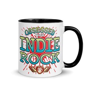 May include: White ceramic mug with a black interior and handle. The mug features the text "OBSESSED WITH INDIE ROCK" in a colorful design with a monkey logo with wings. The design is set against a red burst background.