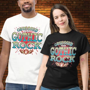 Puede incluir: Dos camisetas, una blanca y otra negra, con el texto "Obsessed with Gothic Rock" en un diseño retro colorido. El diseño incluye una explosión roja, texto azul y amarillo, y un gráfico de mono alado.