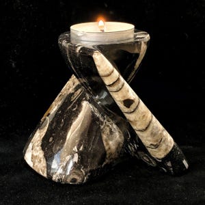 May include: A black and white stone candle holder with a lit tea light candle. The candle holder has a unique, twisted design with a natural, marbled pattern. The candle holder is made of stone and has a polished finish.