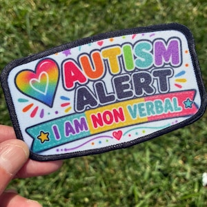 May include: A rectangular patch with a black border featuring a rainbow-colored heart and the text AUTISM ALERT in bold letters. Below, a banner contains the text I AM NON VERBAL in colorful letters, accented by small stars and dots.