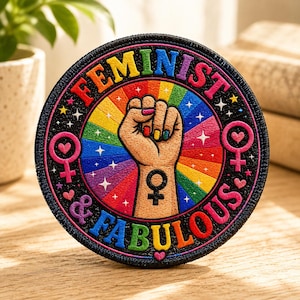 May include: Round patch with the words "FEMINIST & FABULOUS" in rainbow colors. The patch features a raised fist with rainbow-colored nails, set against a rainbow background. Pink hearts and the female symbol are also included.