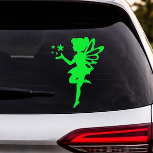 May include: A bright green fairy sticker applied to a car window. The fairy has wings and is holding stars. The sticker is a silhouette design, with the fairy's form and the stars cut out of the green material.